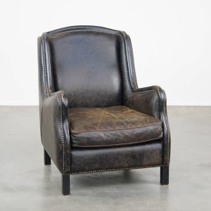 Karaktervolle, stoere zwarte rundleren fauteuil met een hoge rug en afgewerkt met siernagels, industriële stijl