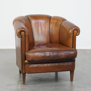 Unieke vintage cognac kleurige lederen clubfauteuil met een goed zitcomfort en een afwerking met zwarte biezen