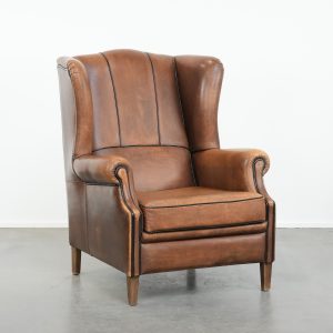 Schapenleren oorfauteuil met mooie kleuren en een luxe afwerking met zwarte biezen in een goede staat