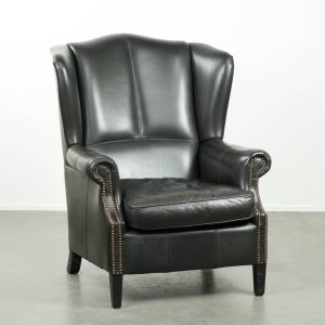 Zwarte rundleren oorfauteuil in een klassiek Engelse stijl afgewerkt met siernagels