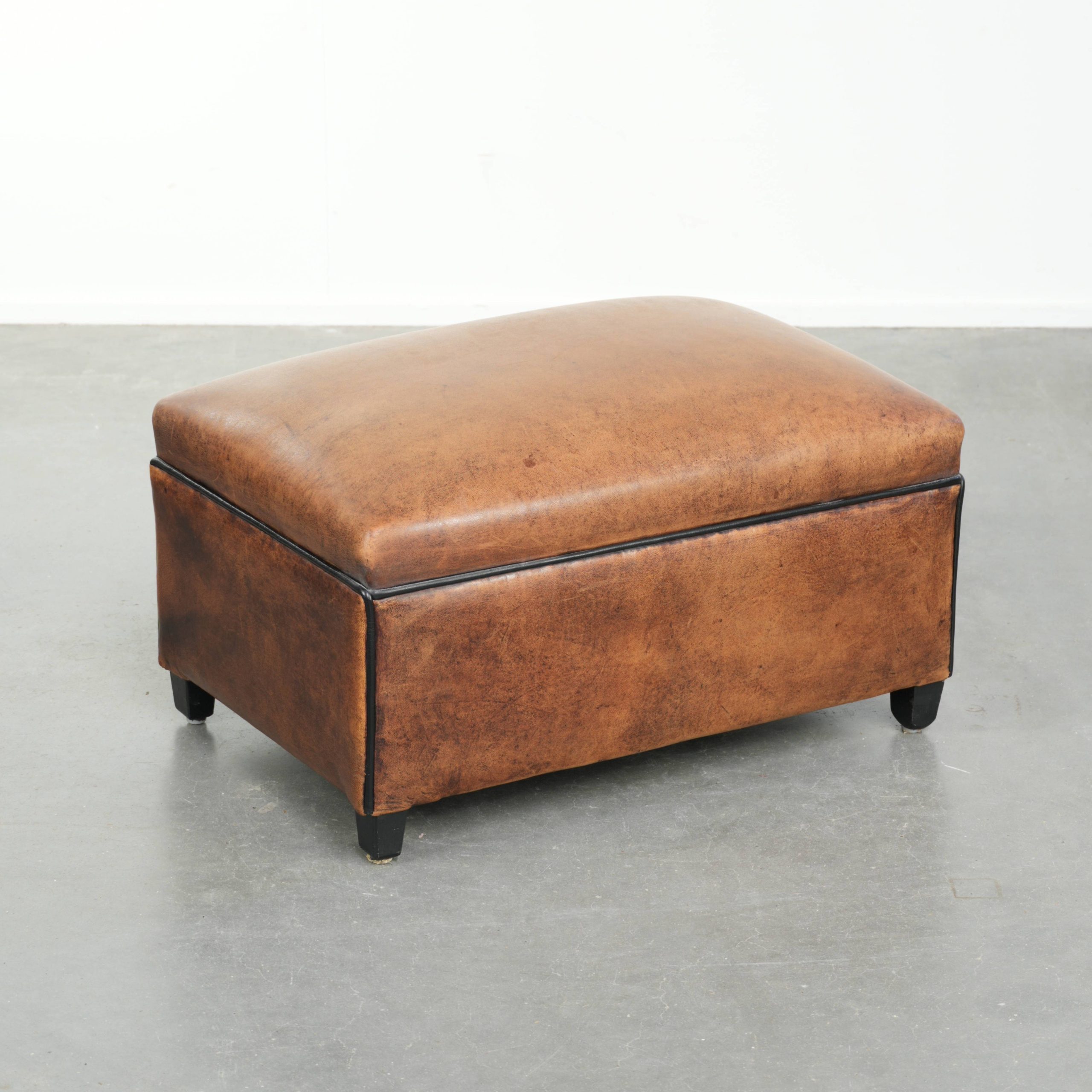 Karaktervolle schapenleren voetenbank/ hocker met mooi patina en afgewerkt met zwarte biezen