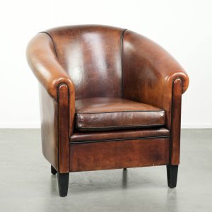 Mooie en karaktervolle schapenleren clubfauteuil met mooie diepe warme kleuren, zwarte biezen en een comfortabele zit