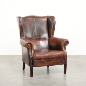 Ruime vintage schapenleren oorfauteuil in een diepe bruine kleur afgewerkt met siernagels