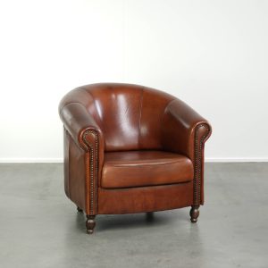 Schapenleren clubfauteuil in een warme cognac kleur afgewerkt met siernagels en een correcte zit