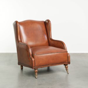 Schapenleren armchair in Engelse stijl in een warme cognac kleur afgewerkt met zwarte biezen en wieltjes