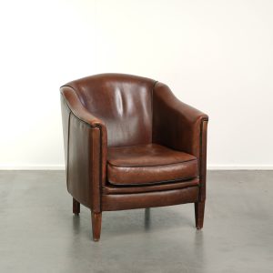 Subtiele schapenleren armchair in een diep bruine kleur afgewerkt met zwarte biezen