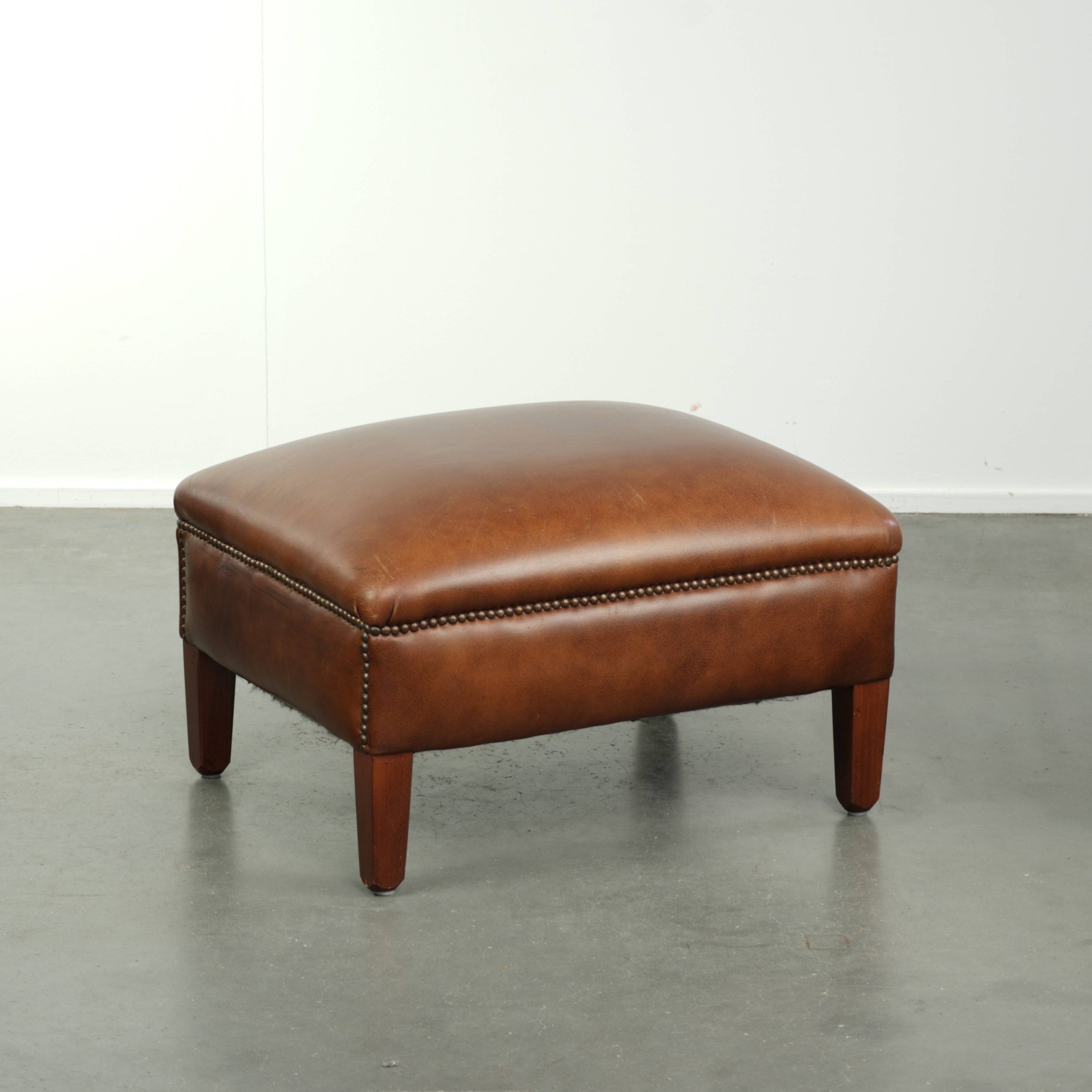 Rundleren hocker in een warme cognac kleur afgewerkt met siernagels