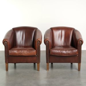 Set van 2 schapenleren clubfauteuils in een donkere cognac kleur afgewerkt met siernagels